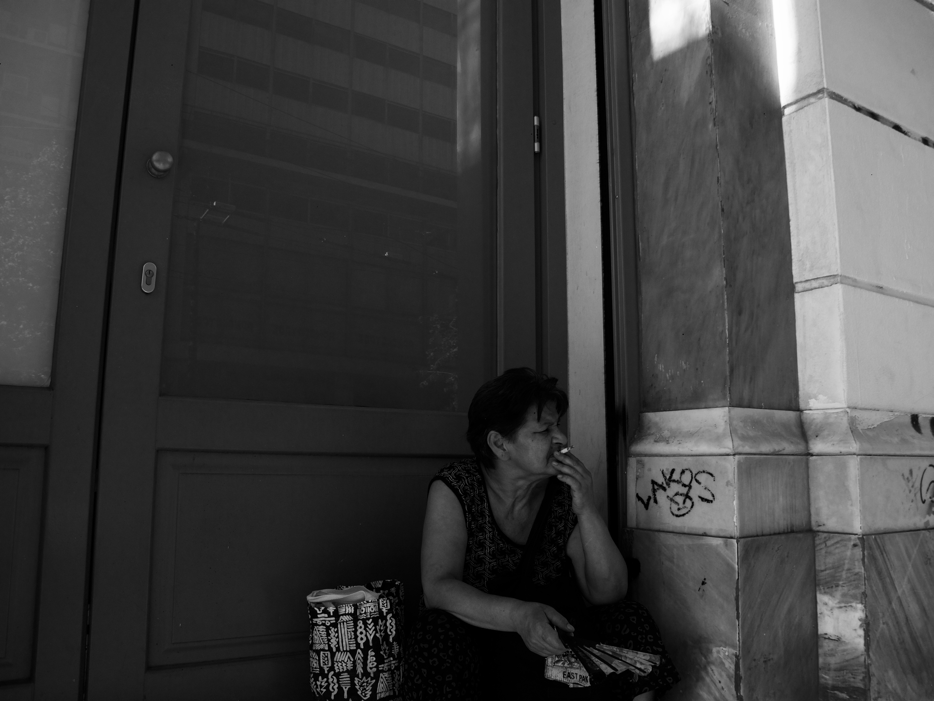 Photo of a woman sitting and smoking by a building